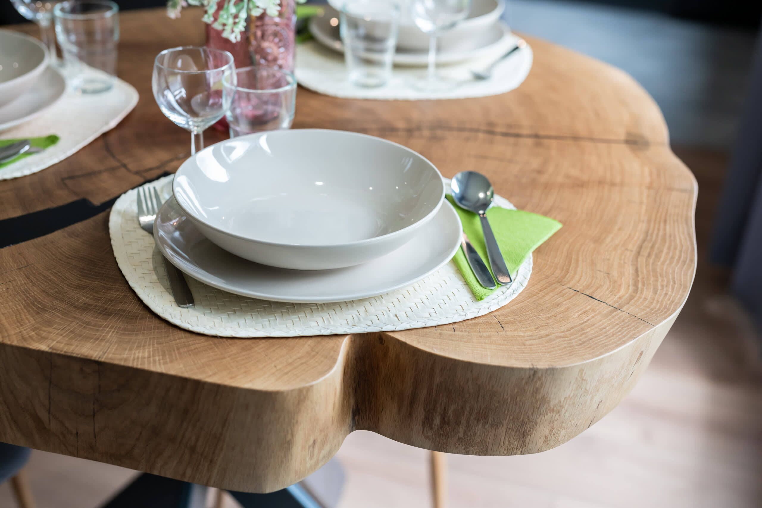 Una mesa de madera con un bol blanco, una servilleta verde y una cuchara.