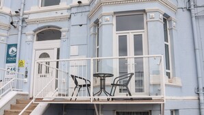 A blue building with a balcony, white railings, and a staircase leading to the entrance.