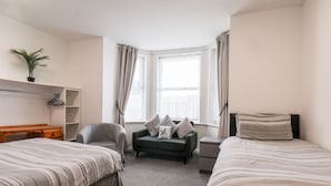 A hotel room with two single beds, a desk, a chair, a small sofa, and a window with curtains.