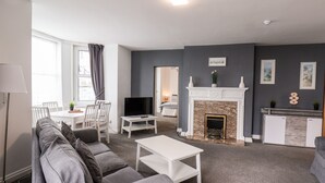 A modern living room with a grey sofa, white coffee table, and a fireplace.