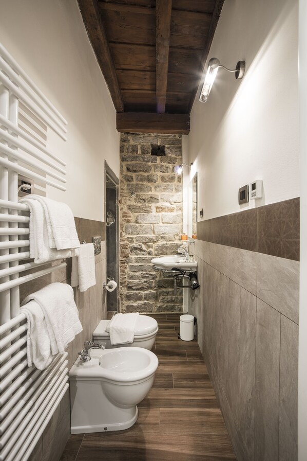 A narrow bathroom with a stone wall, a white sink, a bidet, and a towel rack. - Residenza delle arti (Florence)