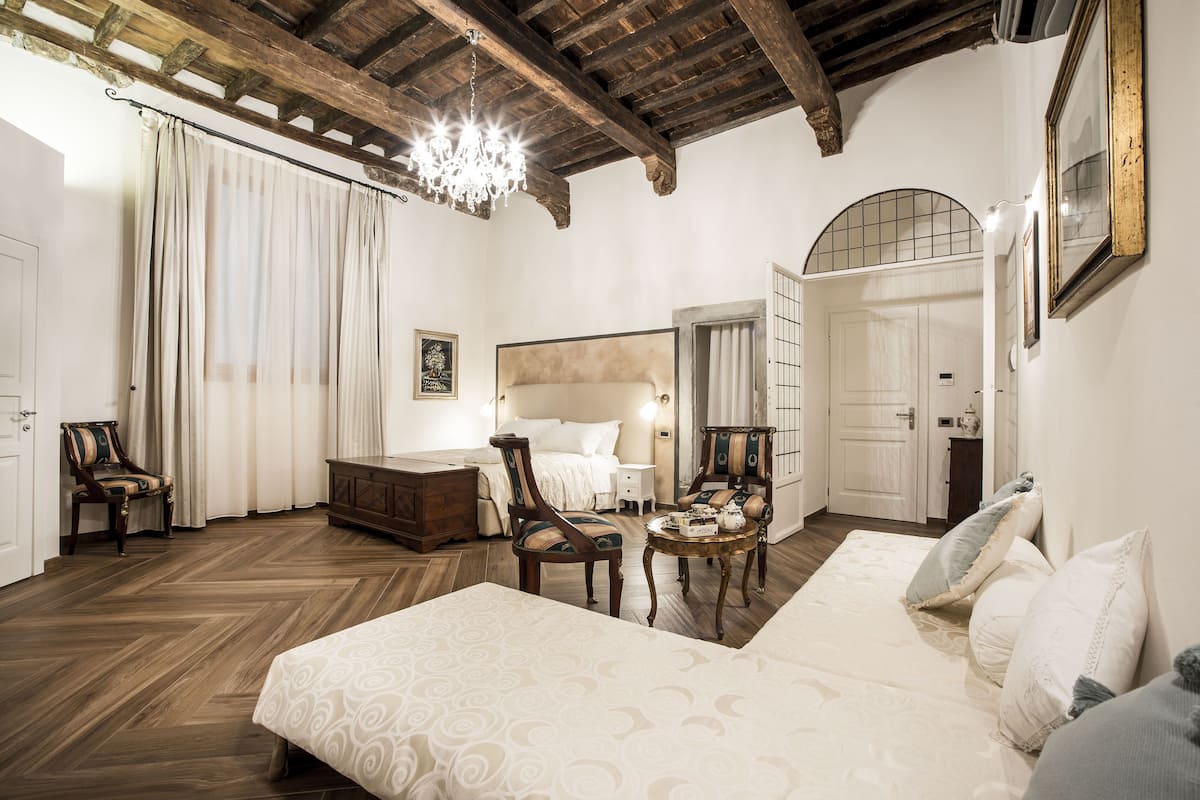 A room with a bed, two chairs, a small table, and a chandelier.