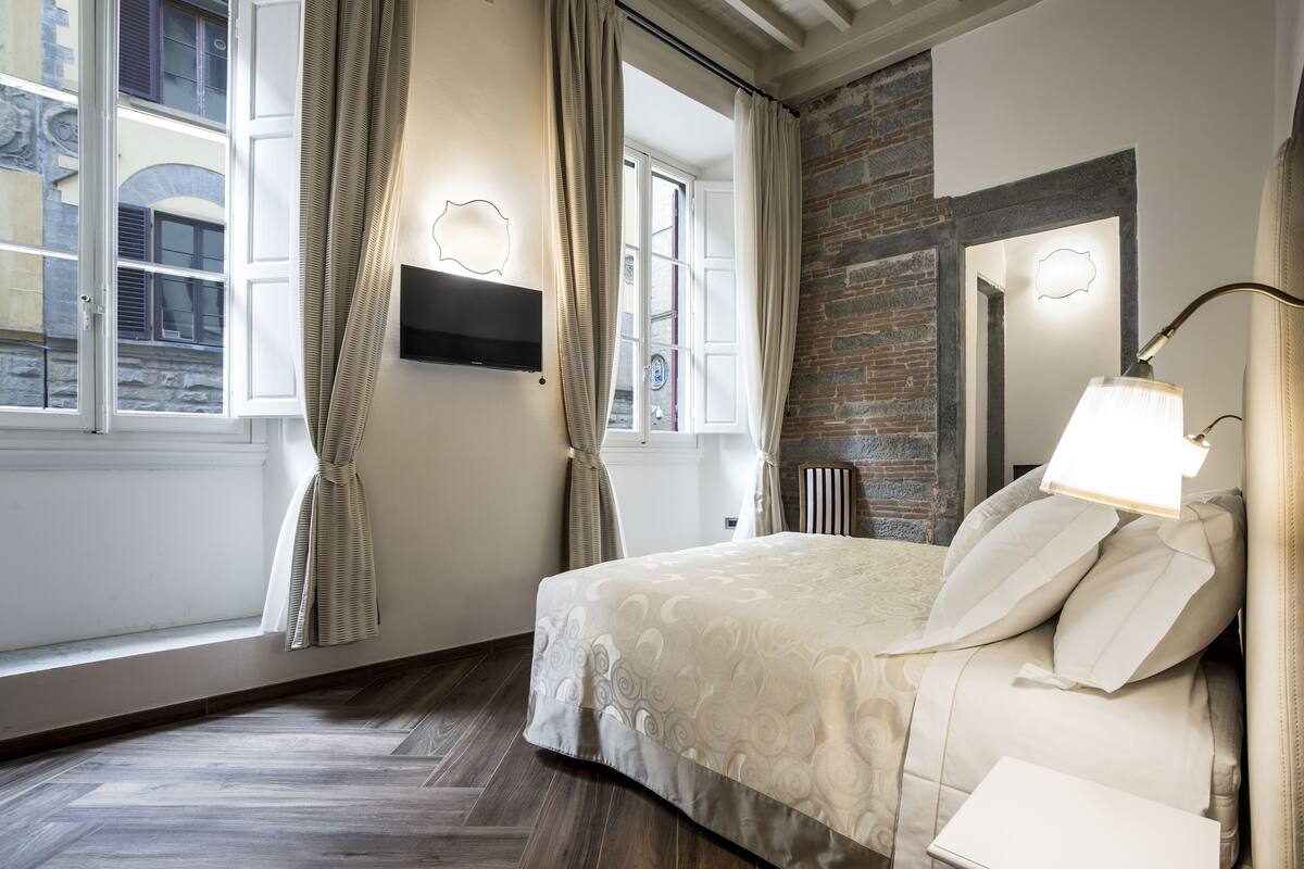 A bedroom with a bed, a TV mounted on the wall, and a window with curtains.