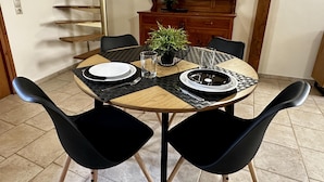 A dining area with a round table, black chairs, a potted plant, and a wooden cabinet in the background. - City Center 1-bed House in Heraklion (Heraklion)