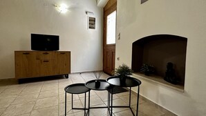 A living room with a TV on a wooden cabinet, a fireplace, and a small table with chairs. - City Center 1-bed House in Heraklion (Heraklion)