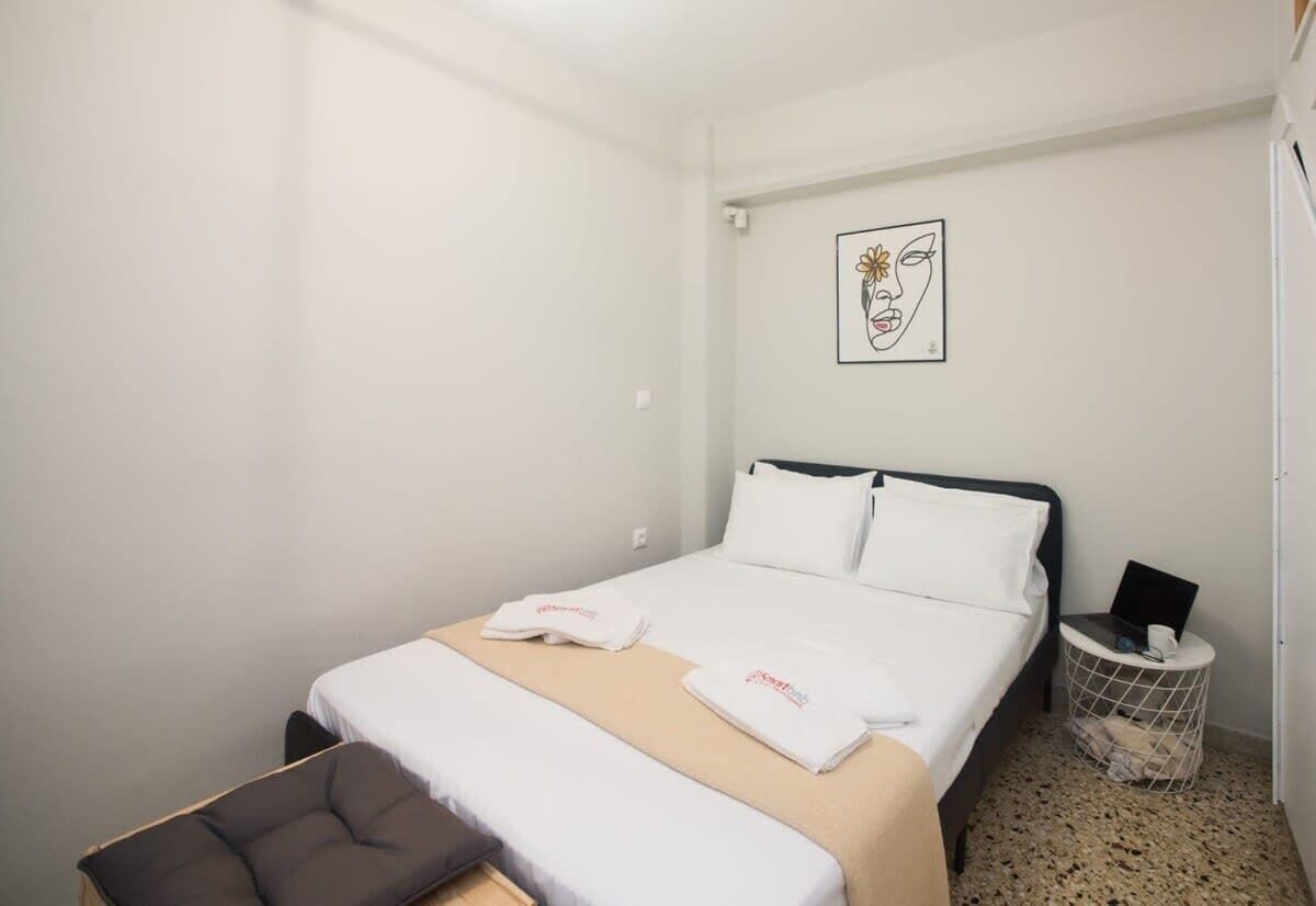 A neatly arranged hotel room with a bed, a small seating area, and a bedside table with a laptop and a cup.