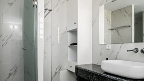 A modern bathroom with a marble shower, a white sink, and a large mirror.
