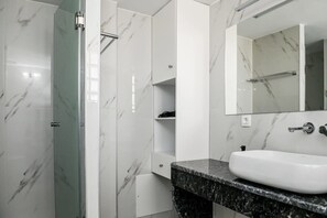 A modern bathroom with a marble shower, a white sink, and a large mirror.