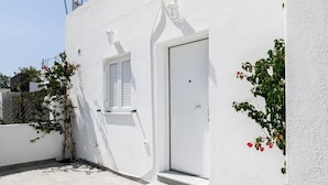 A white building with a door and a window, a small set of steps, and a wall-mounted light fixture. - Santorini Life Vibrant Studio Only 50m from the Beach (Perissa Santorini)