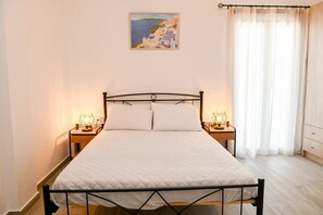 Uma cama de solteiro com estrutura de metal, duas mesas de cabeceira com abajures, um quadro na parede e uma janela com cortinas.