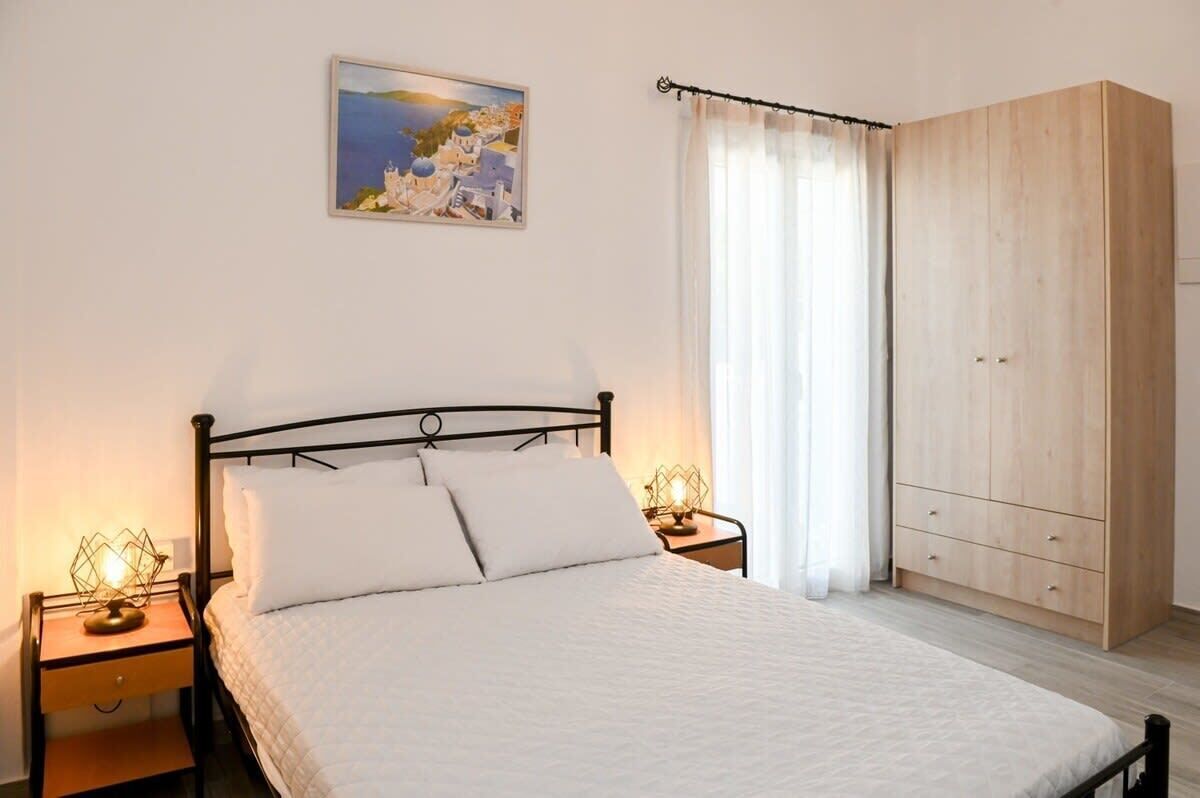 A bedroom with a bed, two bedside tables, a nightstand, a wardrobe, a painting on the wall, and a window with curtains.