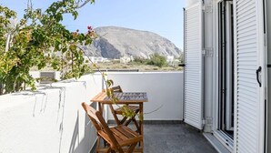 A balcony with a wooden table and chairs, a white wall, and a view of a mountain.