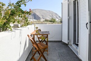 A balcony with a wooden table and chairs, a white wall, and a view of a mountain.