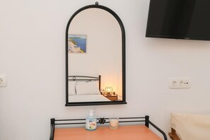 Une chambre à coucher avec un lit, une table de chevet avec une lampe, un miroir et un téléviseur fixé au mur.