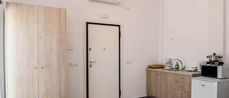 A compact kitchen with a microwave, a small refrigerator, and a wooden wardrobe.