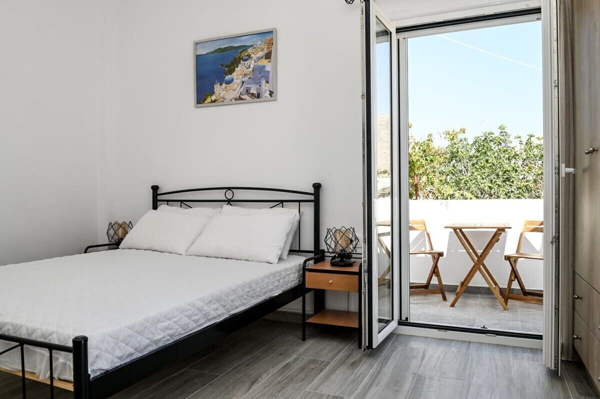 A bedroom with a bed, a nightstand, a painting, and a sliding glass door leading to an outdoor seating area.