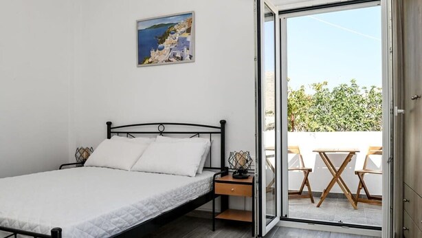 A bedroom with a bed, a nightstand, a painting, and a sliding glass door leading to an outdoor seating area.