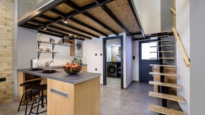 A modern kitchen with a central island, bar stools, and a built-in washing machine. - Loft 2 (Kos)