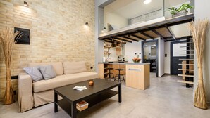 A modern living room with a sofa, coffee table, and a kitchen area in the background. - Loft 2 (Kos)