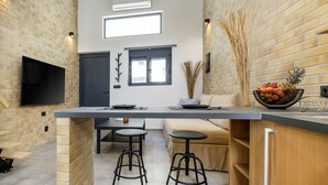 A modern kitchen with a built-in TV, two stools, a dining table, and a fruit bowl. - Loft 2 (Kos)