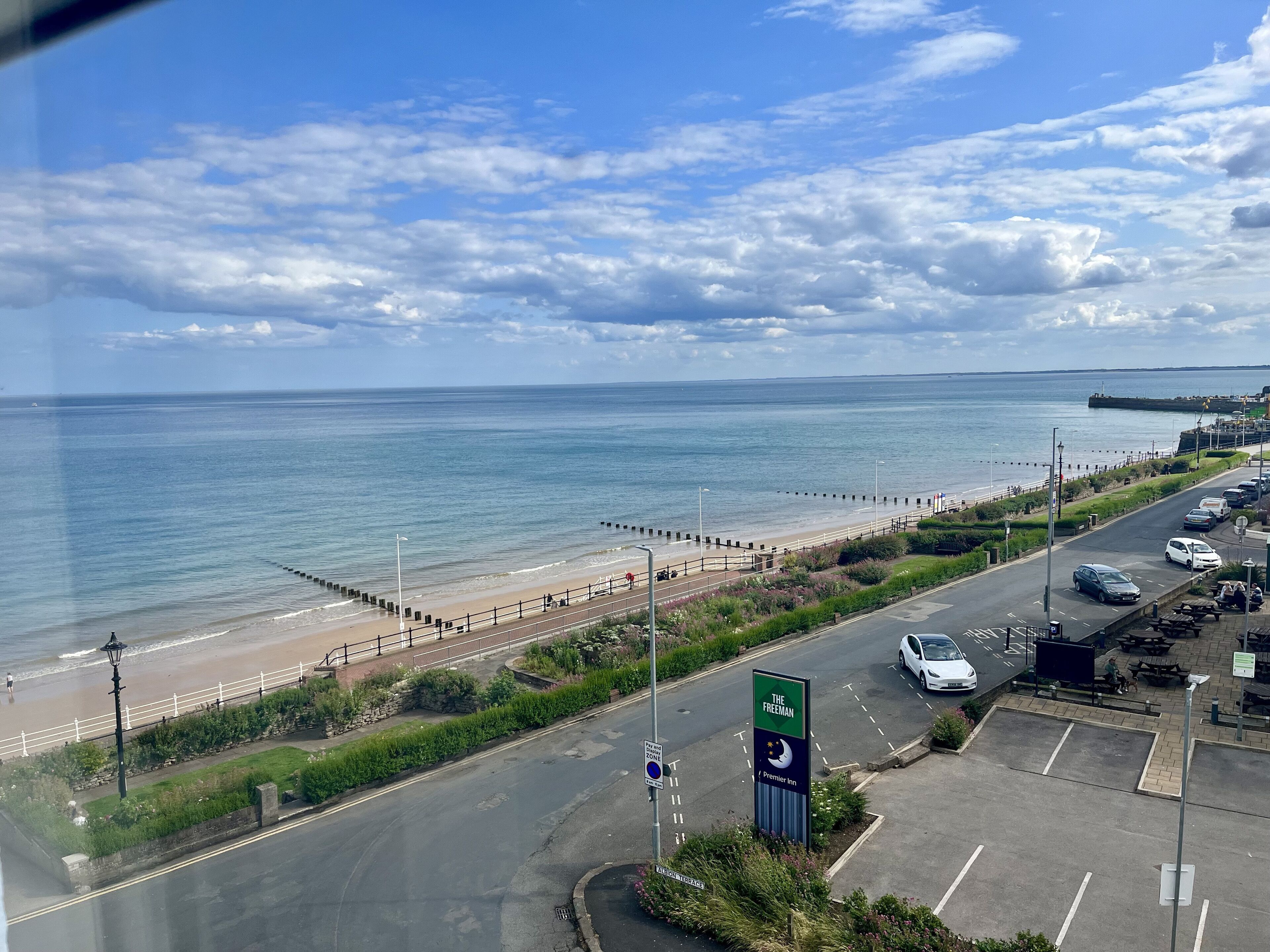 Una carretera costera con una playa, un paseo marítimo y un cartel de hotel que indica 'The Freeman'.