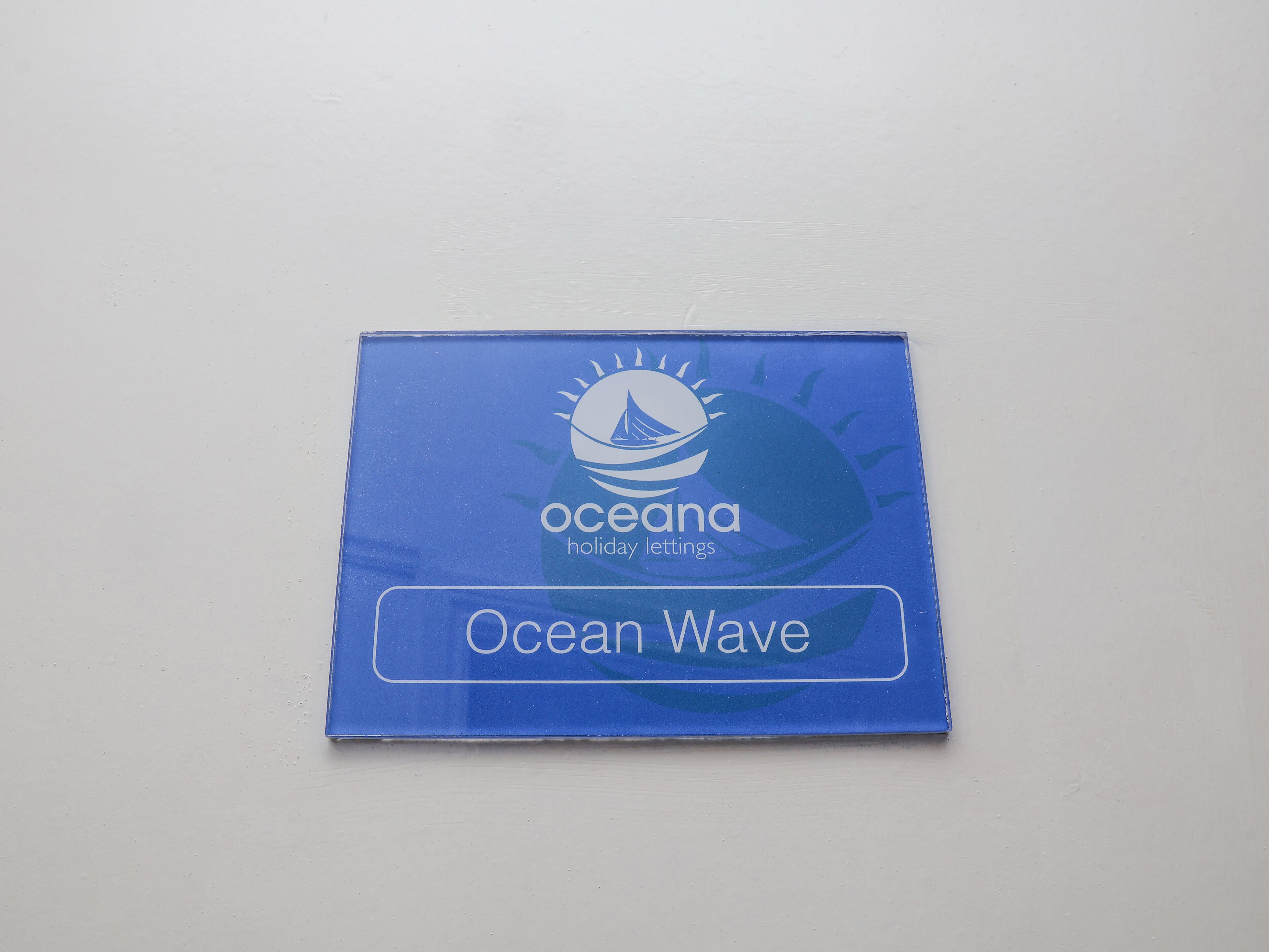 A blue sign with the text "oceanana holiday lettings" and "Ocean Wave" on a white background.