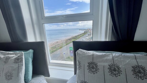 A room with two beds, a window with a view of the beach and sea, and a sign for 'The Helga'. - Ocean Wave (Bridlington)