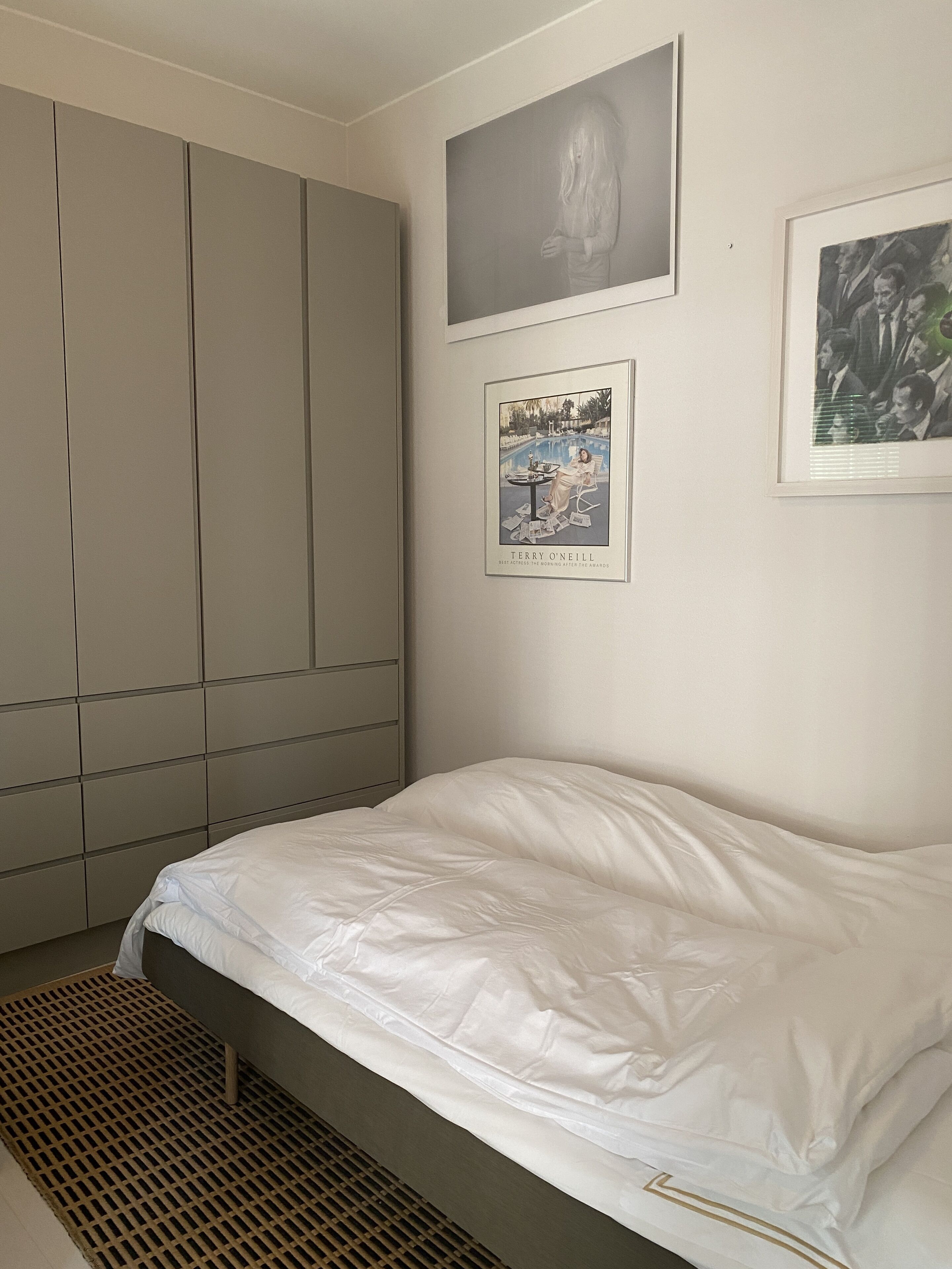 A bedroom with a bed, a wardrobe, and two framed pictures on the wall.