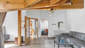 A spacious living area with a wooden ceiling, a glass coffee table, a grey sofa, and a dining area in the background. - 2 bedroom apartment in buchenberg (Buchenberg)