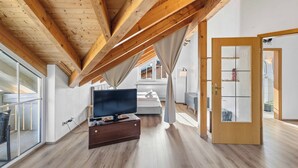 A modern living room with a wooden ceiling, a flat-screen TV on a wooden stand, a sofa, and a large window. - 2 bedroom apartment in buchenberg (Buchenberg)