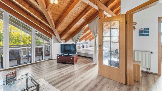 A spacious room with a high ceiling, wooden beams, a large window, a bed, a TV, and a glass table. - 2 bedroom apartment in buchenberg (Buchenberg)