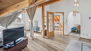 A spacious room with a large flat-screen TV on a wooden dresser, a ceiling with exposed beams, and a modern chandelier. - 2 bedroom apartment in buchenberg (Buchenberg)