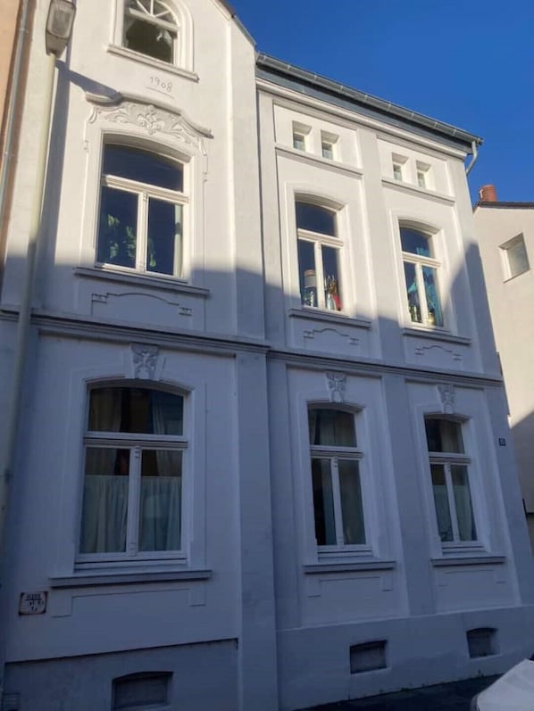 A white building with multiple windows, a date plaque reading "1908", and a small sign indicating "Hall".