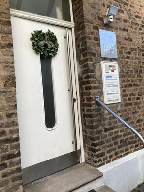 A white door with a green wreath, a sign reading "15 HAUS FRIEDA", and a utility box with a metal handle.