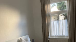 A double bed with white bedding, a bedside table, a nightstand, and a window with curtains. - 1 Bedroom Apartment in Bonn (Bonn)