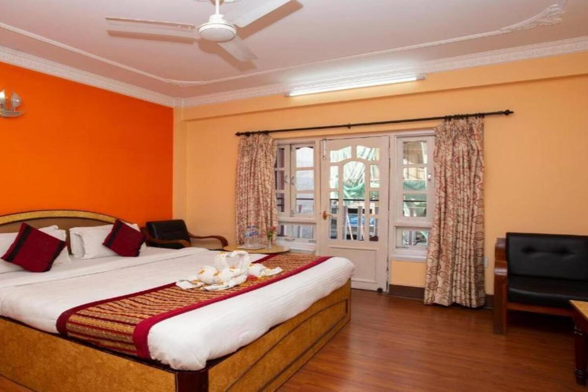 A hotel room with a bed, a nightstand, a chair, a table, a ceiling fan, and a window with curtains.