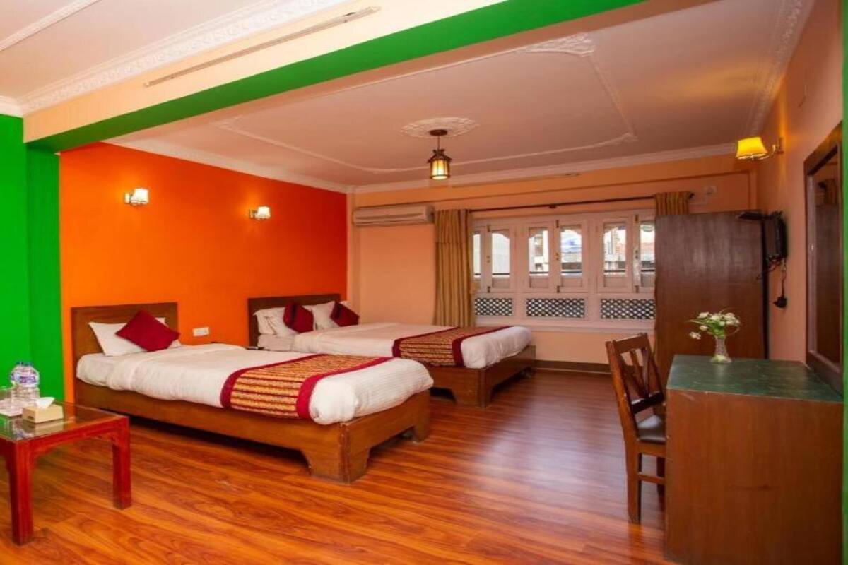 A hotel room with two beds, a wooden floor, a small table with a vase, and a chair.