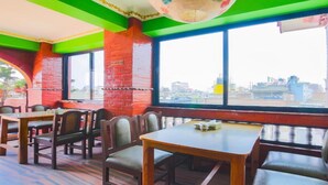A restaurant with wooden tables and chairs, large windows, and a view of the cityscape. - MeroStay 201 MD HOTEL (Kathmandu)