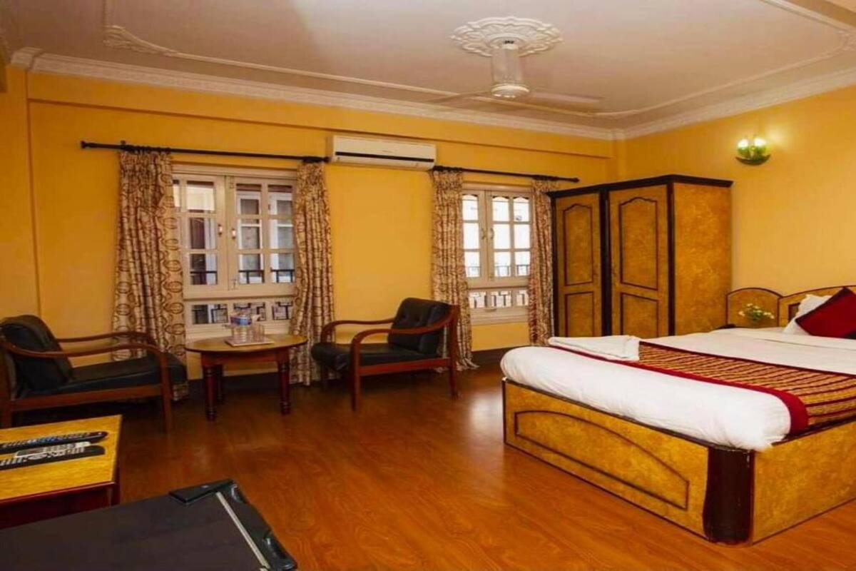 A hotel room with a large bed, a desk, two chairs, and a window with curtains.