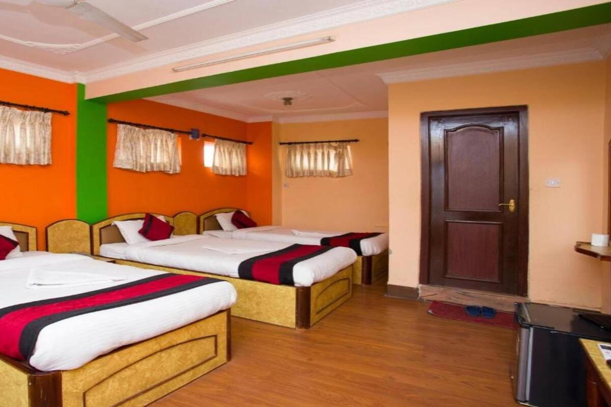 A hotel room with three single beds, a wooden wardrobe, a desk with a chair, and a door.