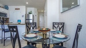 A dining area with a round glass table, black chairs, and a central decorative bowl. A kitchen with white cabinets and a stainless steel refrigerator is visible in the background. - Outstanding Oceanfront unit with a Breathtaking View - Sonoran Sun E-511 (Puerto Peñasco)