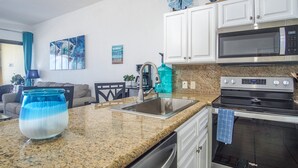 A kitchen with white cabinets, a stainless steel sink, a microwave, and an oven. There is a blue water dispenser and a large blue vase on the counter. - Outstanding Oceanfront unit with a Breathtaking View - Sonoran Sun E-511 (Puerto Peñasco)