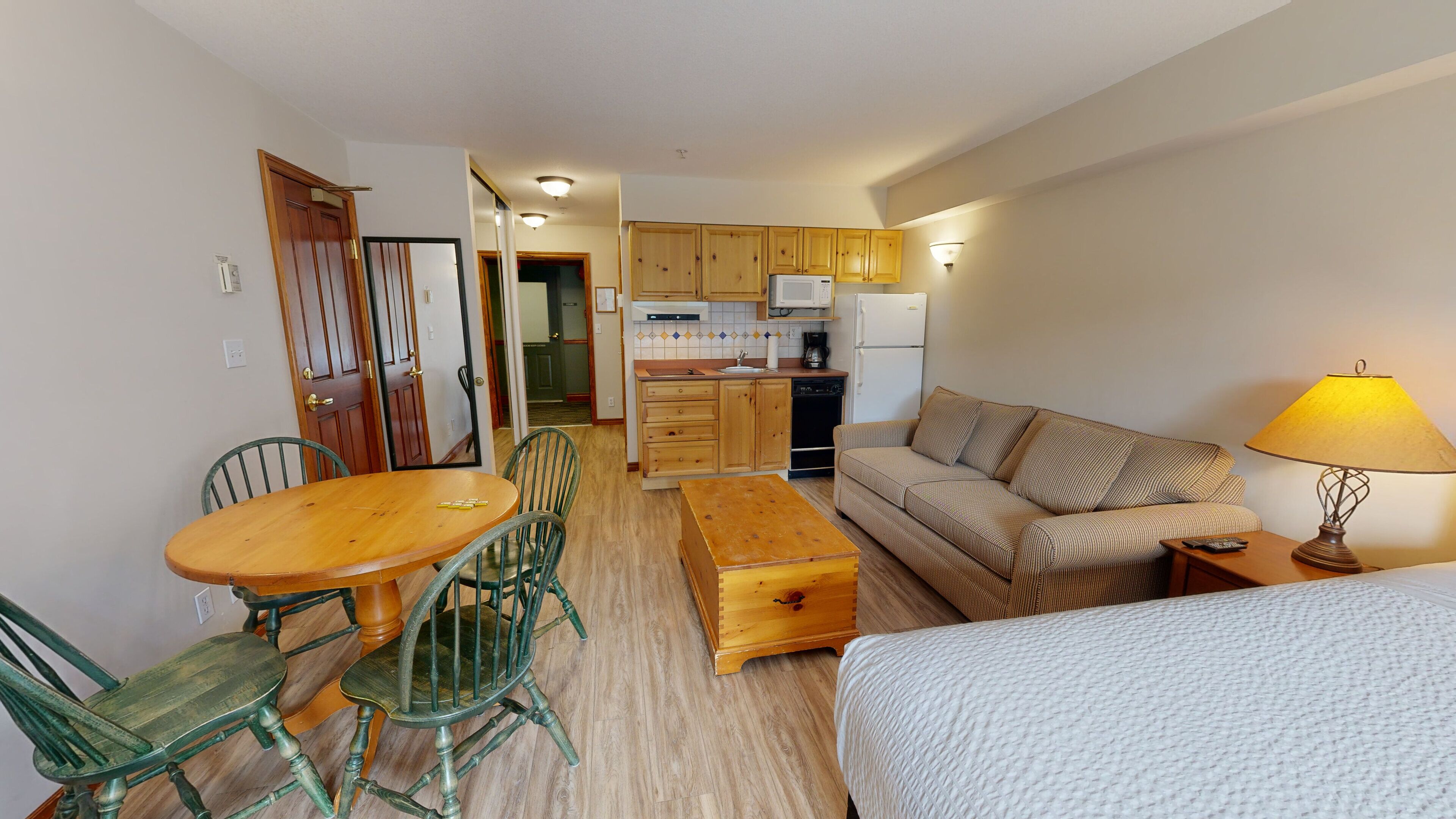 Een ruimtelijk ingerichte leefruimte met een kitchenette, een eethoek met een houten tafel en stoelen, een bank en een bed.