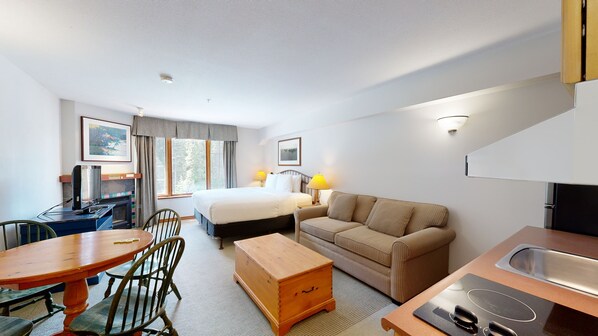 Habitación de hotel con cama, sofá, escritorio con ordenador, mesa de comedor con sillas y kitchenette.