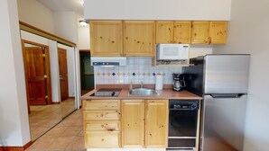 Cocina compacta con armarios de madera, microondas, cafetera y lavavajillas.