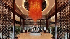 A lobby with a central reflective sculpture, patterned wooden screens, and a circular ceiling light fixture. - Ondine Oriental International Hotel (Zhenjiang)