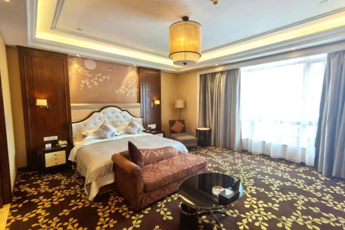 Una habitación de hotel con una cama grande, un sofá marrón, una mesita y un candelabro.
