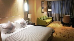 A hotel room with a bed, a green sofa, a desk with a chair, and a large window with curtains. - Ondine Oriental International Hotel (Zhenjiang)
