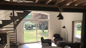 Un salon moderne avec un escalier, un coin repas avec une table ronde et des chaises, et une grande porte-fenêtre coulissante donnant sur un jardin.