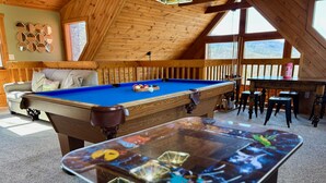 Een houten interieur met een pooltafel, een biljarttafel en een bank.